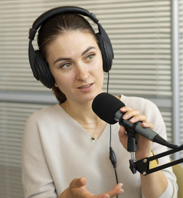 Jessica Jung, podcast host, wearing headphones and speaking into a microphone in a recording studio setting.