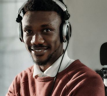 Smiling audio host wearing headphones, posing in a studio setting, representing Blueprints and Beginnings' diverse audio content.