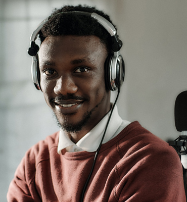 Young man wearing headphones, smiling, in a podcast studio setting, representing David Michale, audio host and adviser.