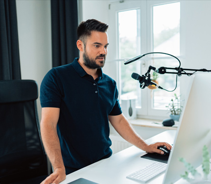 Man engaged in podcasting or online content creation at a desk with a microphone and computer, reflecting the mission of Blueprints & Beginnings to empower individuals through mentorship and actionable insights.