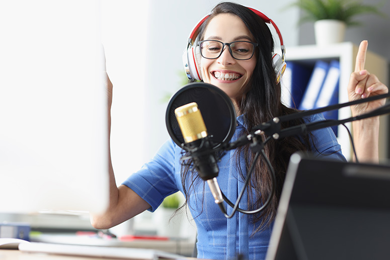 Woman wearing headphones and glasses, smiling while speaking into a microphone, representing podcasting and lifestyle content creation.