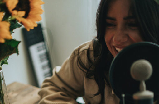 Woman smiling while speaking into a microphone, with sunflowers in a vase on a table, representing engaging podcast content.