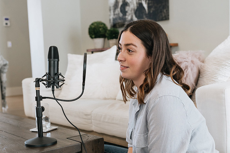 Woman speaking into a microphone in a cozy living room setting, illustrating podcast production and lifestyle content.
