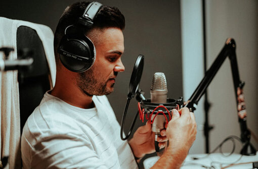 Man adjusting microphone in podcast studio, wearing headphones, preparing for audio recording session related to business discussions.