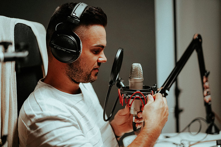 Man adjusting a microphone while wearing headphones in a podcast studio setting, reflecting themes of podcast production and audio content creation.