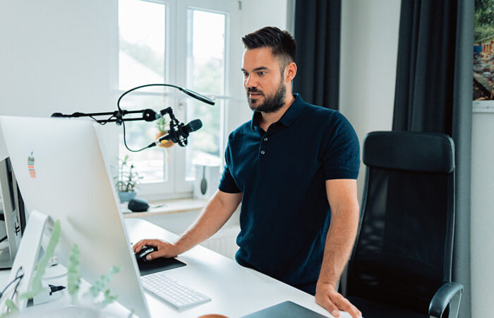 Man standing at a desk with a microphone and computer, preparing for a podcast event related to Rockness Festivals.