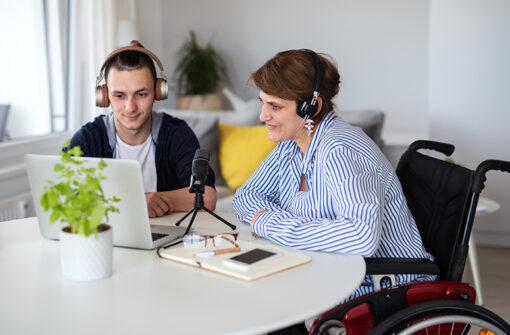 Man and woman with headphones engaged in podcast recording at a table, featuring a laptop, microphone, and a potted plant, emphasizing creative collaboration in lifestyle topics.