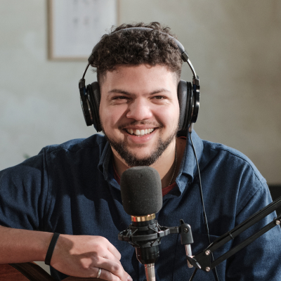 Smiling musician wearing headphones beside a microphone, representing the podcasting and mentorship themes of Blueprints & Beginnings.